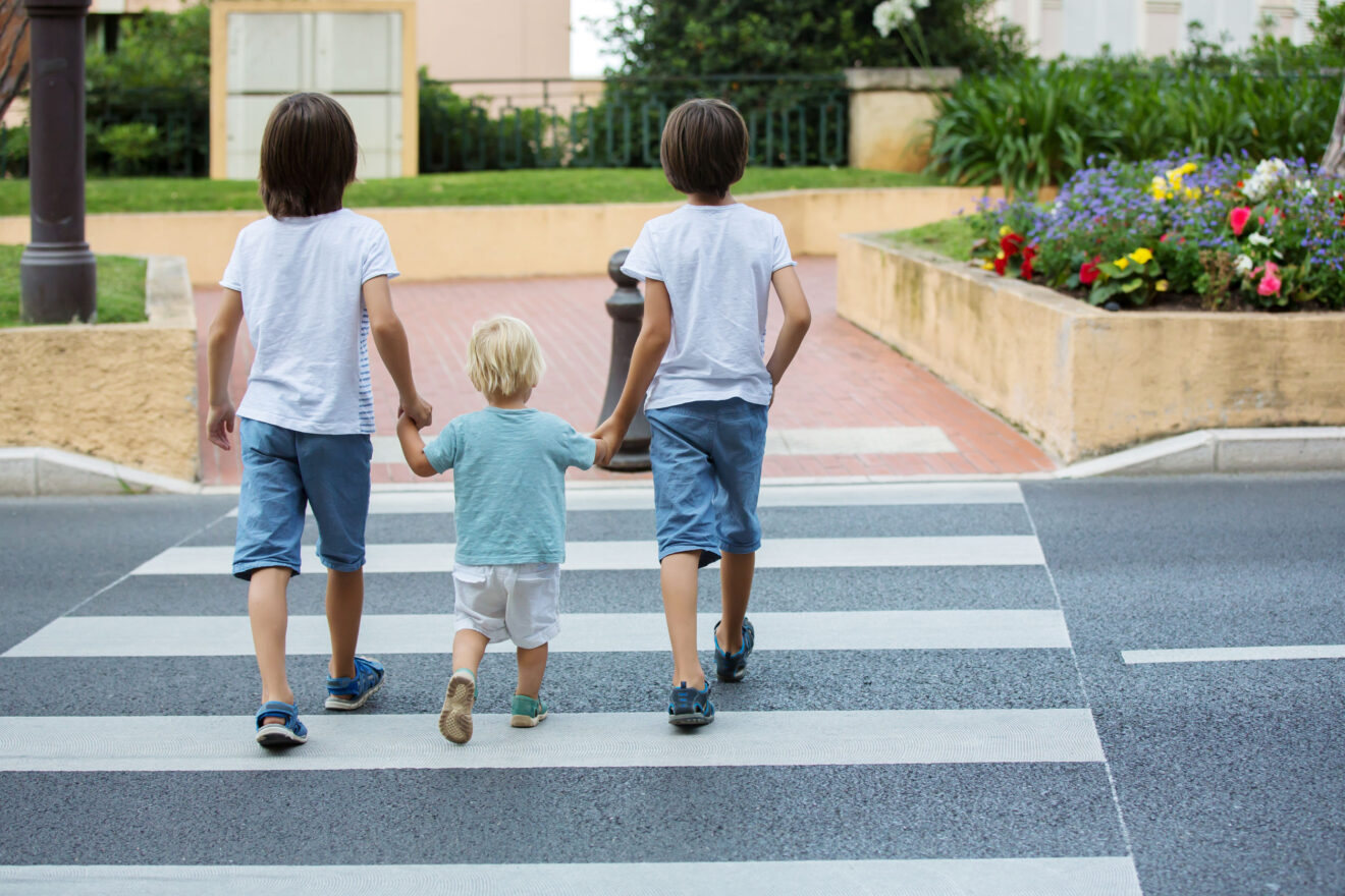 Three children, boys, brothers, holding hands and crossing a str